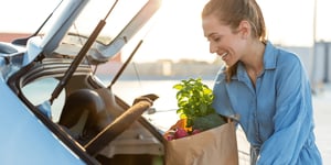 A smiling woman packs her trunk with groceries.